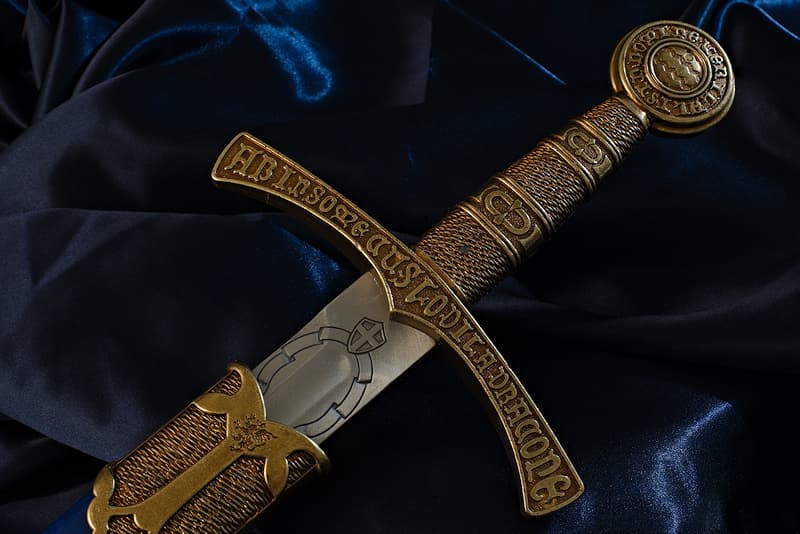 Espada medieval decorativa, hoja grabada, empuñadura y pomo con inscripciones en latín, vaina en azul francés con flor de lis.