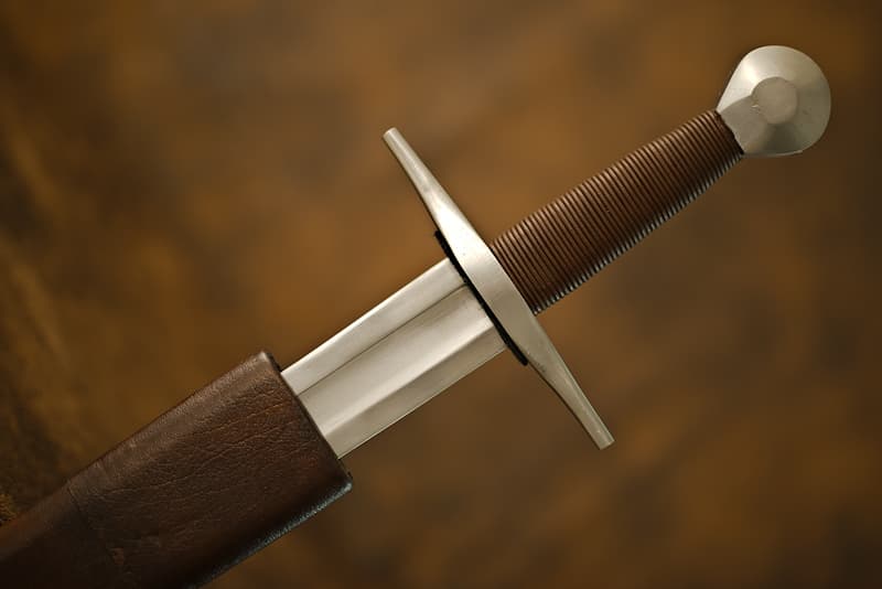 Espada medieval forjada, hoja de garganta corta, empuñadura recubierta de cuero, pomo cilíndrico, vaina de madera y cuero