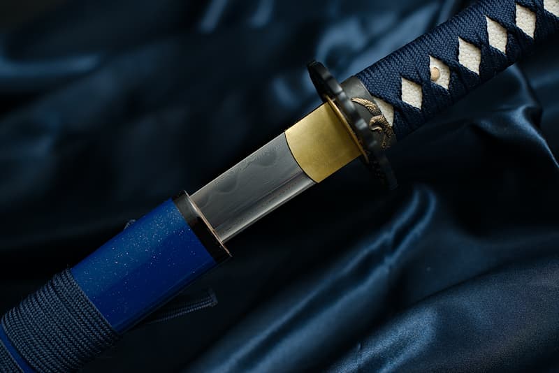 Katana afilada, acero laminado (forja damasco), Hamon auténtico (刃文 línea de endurecimiento), forja, pulida y afilada a mano, saya azul y puntas doradas.