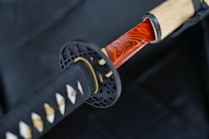 Katana afilada, hoja pintada de rojo y negro, con vaina de madera natural lacada (saya 鞘), sageo negro (下緒) y tsuka-Ito (柄糸) | Algunas personas buscan su propósito toda la vida. Otras exploran, lo encuentran y siguen su camino en armonía.