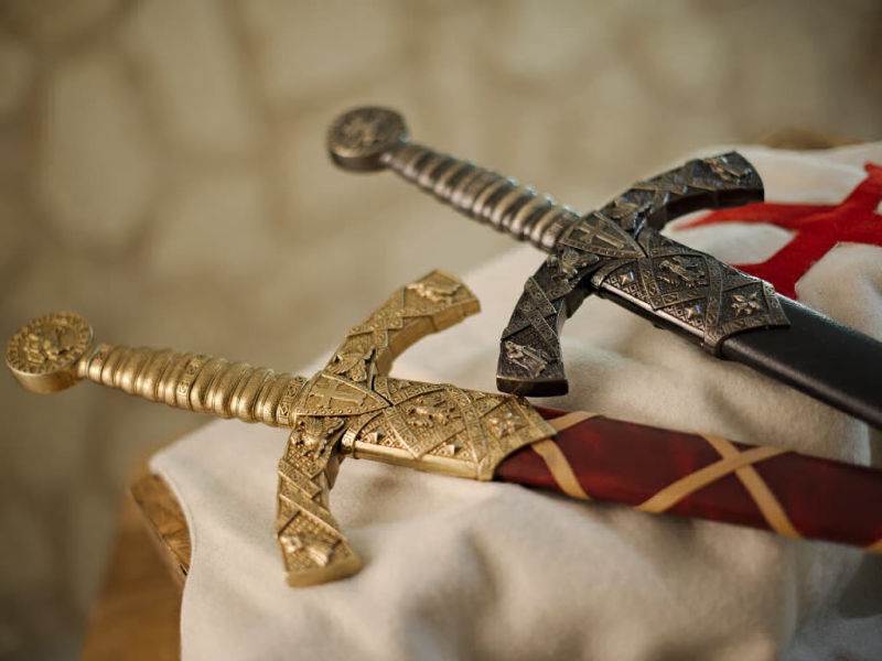 Dos espadas templarias decorativas con vainas rojas trenzadas o negras, montadas sobre un tabardo templario de lana blanca, con la cruz roja templaria patada. Dos espadas templarias decorativas con vainas rojas trenzadas o negras, montadas sobre un tabardo templario de lana blanca, con la cruz roja templaria patada.