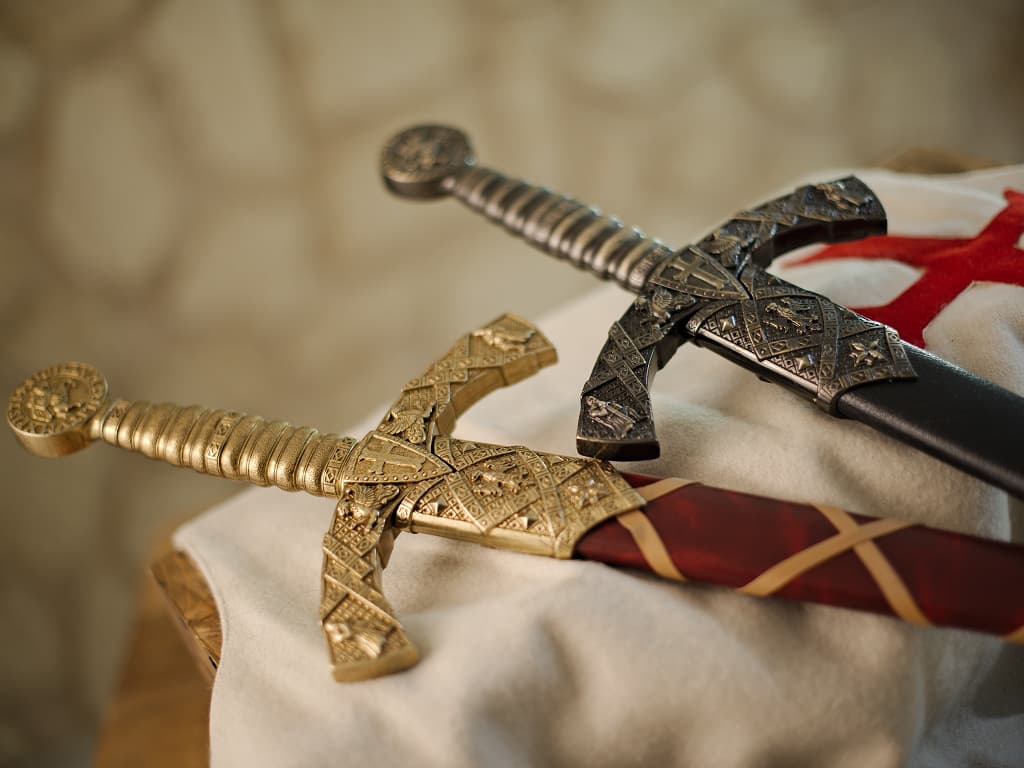 Dos espadas templarias decorativas con vainas rojas trenzadas o negras, montadas sobre un tabardo templario de lana blanca, con la cruz roja templaria patada. Dos espadas templarias decorativas con vainas rojas trenzadas o negras, montadas sobre un tabardo templario de lana blanca, con la cruz roja templaria patada.