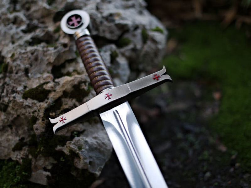 Espada templaria decorativa sobre una roca con fondo de musgo Espada templaria decorativa sobre una roca con fondo de musgo