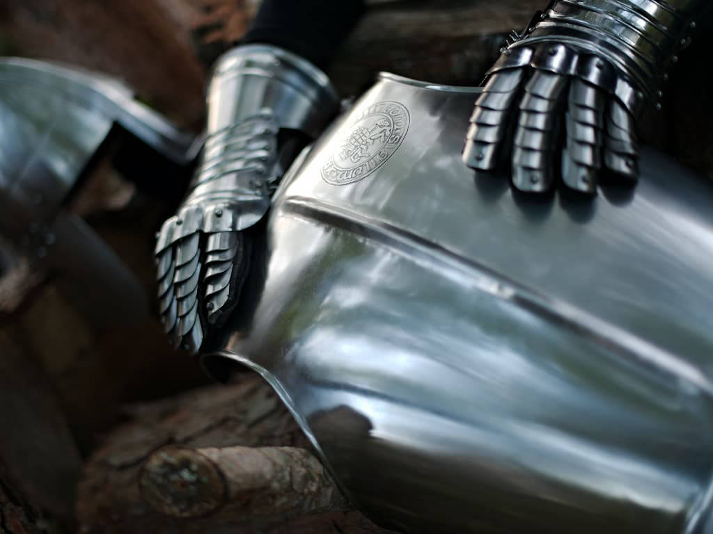 Coraza con el sello templario en relieve, escenificada con un par de guanteletes y un casco medieval Coraza con el sello templario en relieve, escenificada con un par de guanteletes y un casco medieval