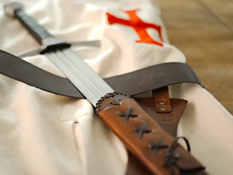 Tabardo templario con espada de combate sobre una mesa de madera medieval Tabardo templario con espada de combate sobre una mesa de madera medieval