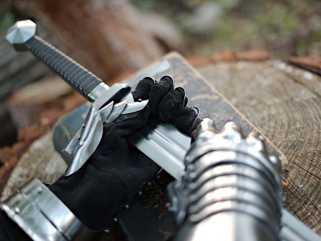 Espada medieval forjada, guanteletes medievales y libro sobre un tronco de árbol