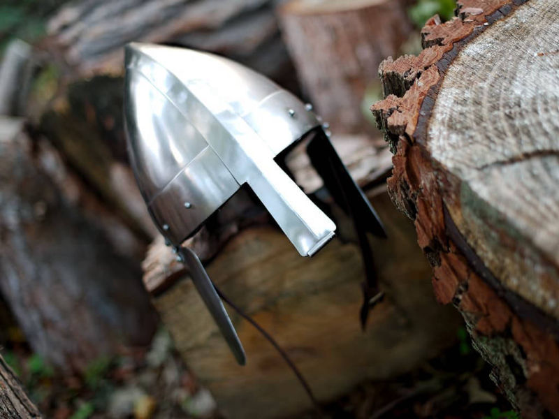 Casco medieval apoyado sobre troncos en un bosque encantado