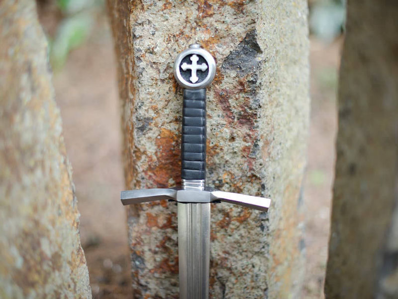 Daga de caballero cruzado medieval engastada sobre piedras naturales verticales Daga de caballero cruzado medieval engastada sobre piedras naturales verticales