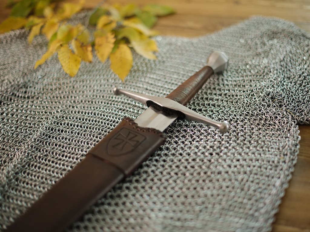 Épée médiévale forgée avec fourreau en bois et cuir, sur une cotte de mailles médiévale Épée médiévale forgée avec fourreau en bois et cuir, sur une cotte de mailles médiévale