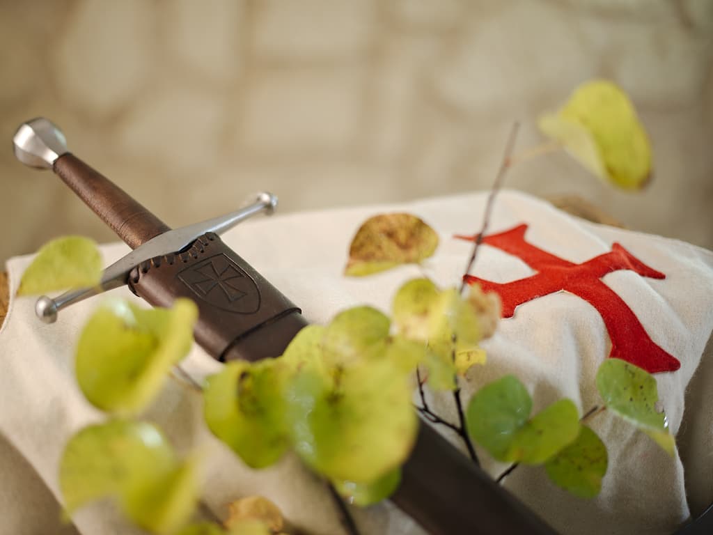 Épée médiévale forgée, posée sur un tabard blanc en laine arborant la croix pattée des templiers Épée médiévale forgée, posée sur un tabard blanc en laine arborant la croix pattée des templiers