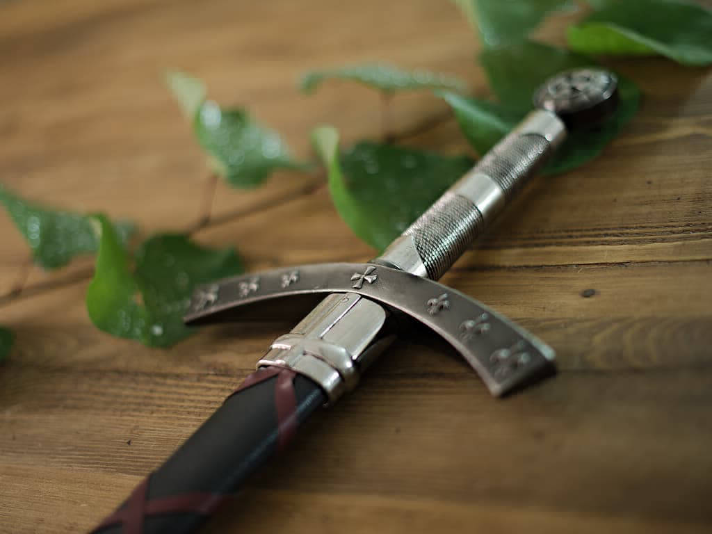 L'épée de la Septième Croisade posée sur une table médiévale en bois, décorée d'une branche végétale avec quelques gouttes de rosée matinale L'épée de la Septième Croisade posée sur une table médiévale en bois, décorée d'une branche végétale avec quelques gouttes de rosée matinale
