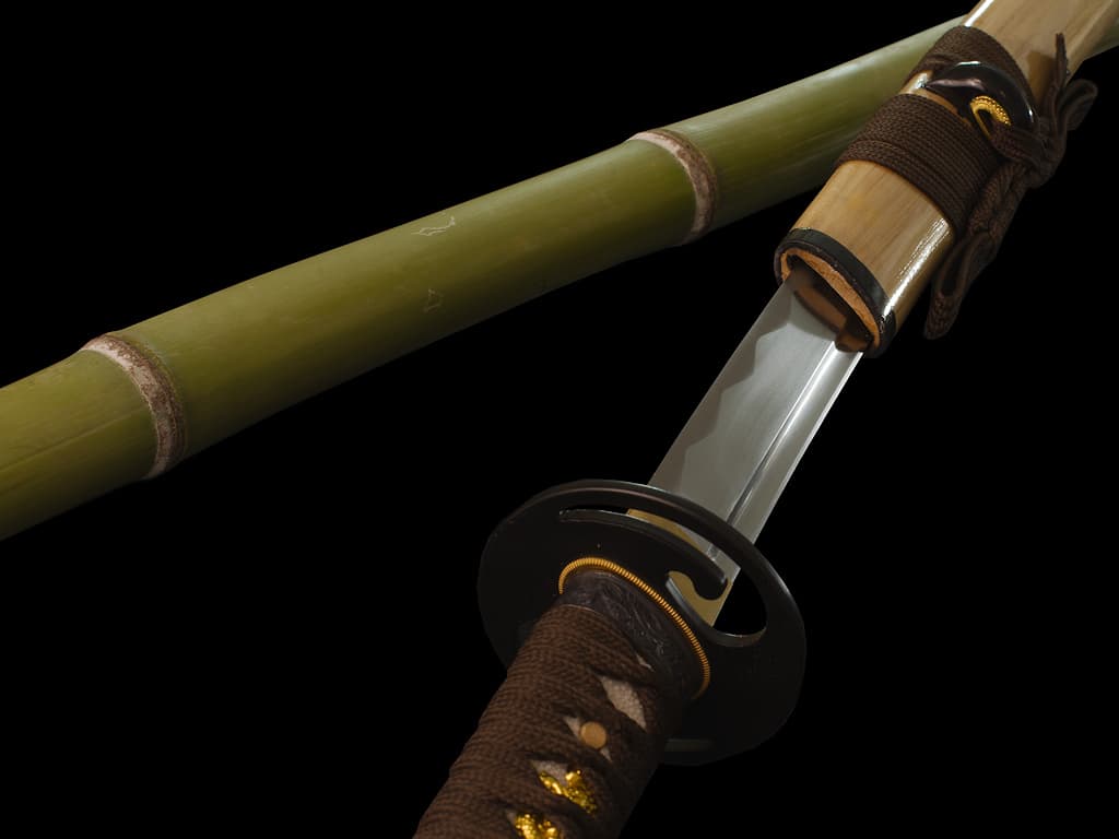 Mù-jīn, wakizashi afilado de madera (mù, 木) metal (jīn, 金): detalle de la hoja saliendo de su vaina (saya), apoyada sobre bambú natural.