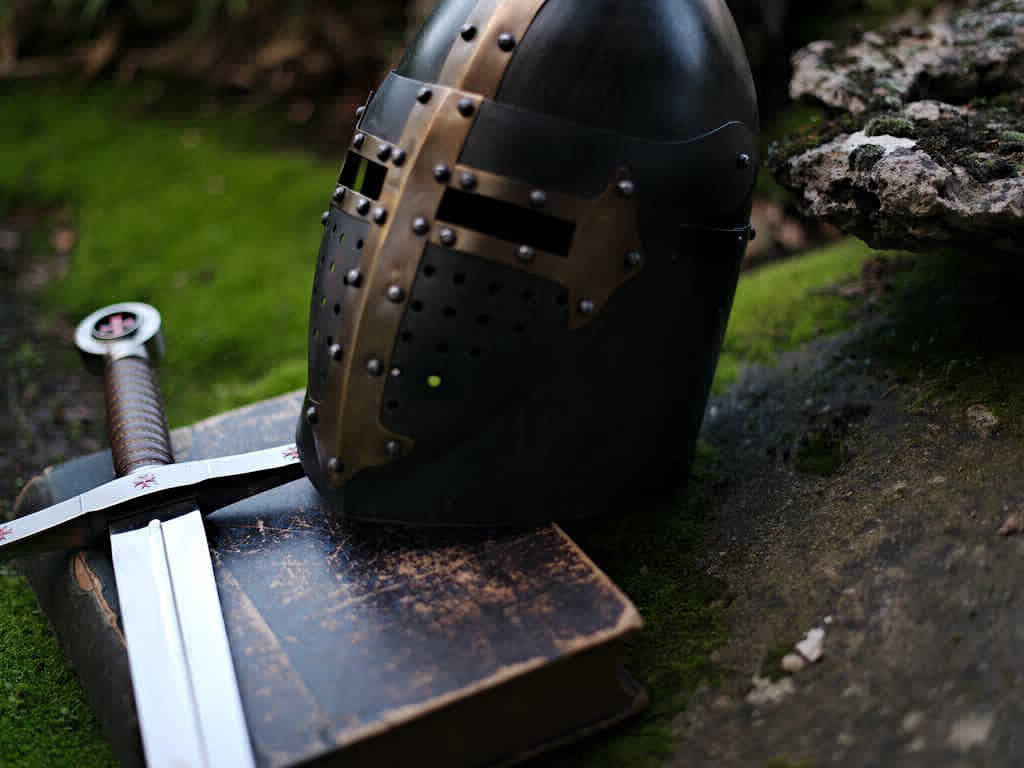 Heaume templier noir avec croix pattée en laiton, posé sur une épée et un livre ancien Heaume templier noir avec croix pattée en laiton, posé sur une épée et un livre ancien