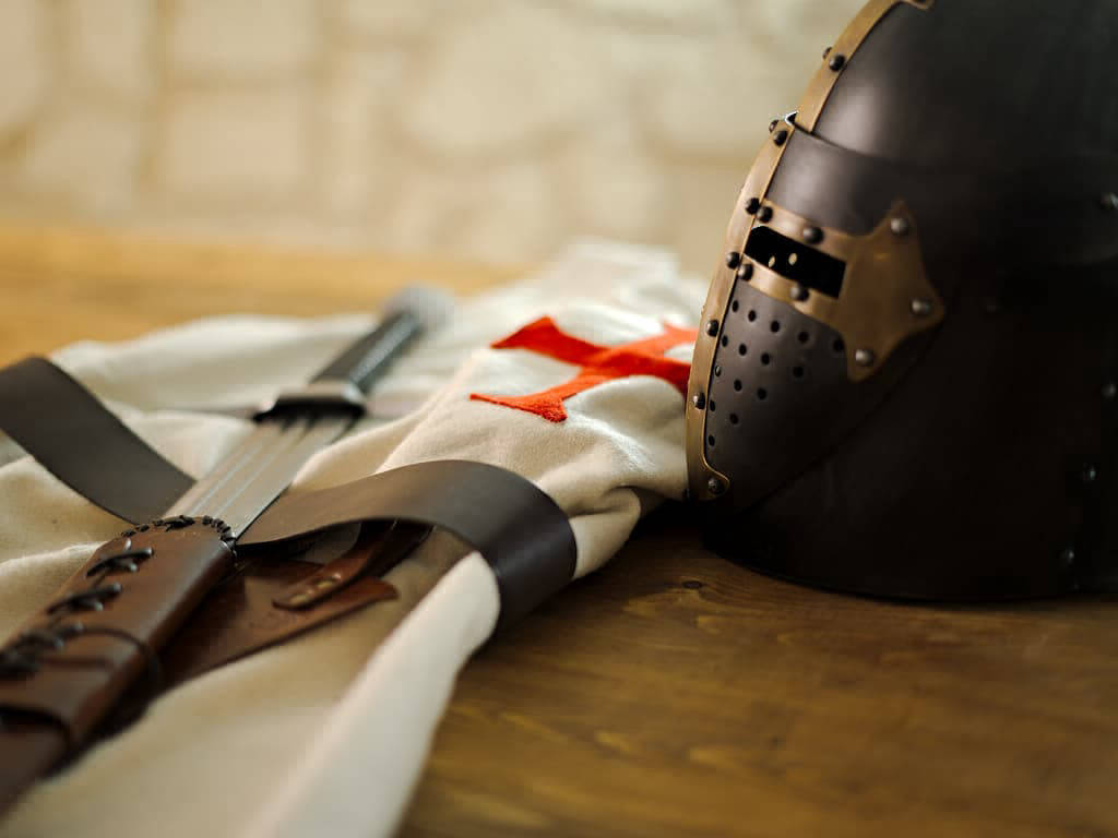 Heaume templier noir posé sur une table médiévale en boir, avec un tabard templier et une épée de combat Heaume templier noir posé sur une table médiévale en boir, avec un tabard templier et une épée de combat