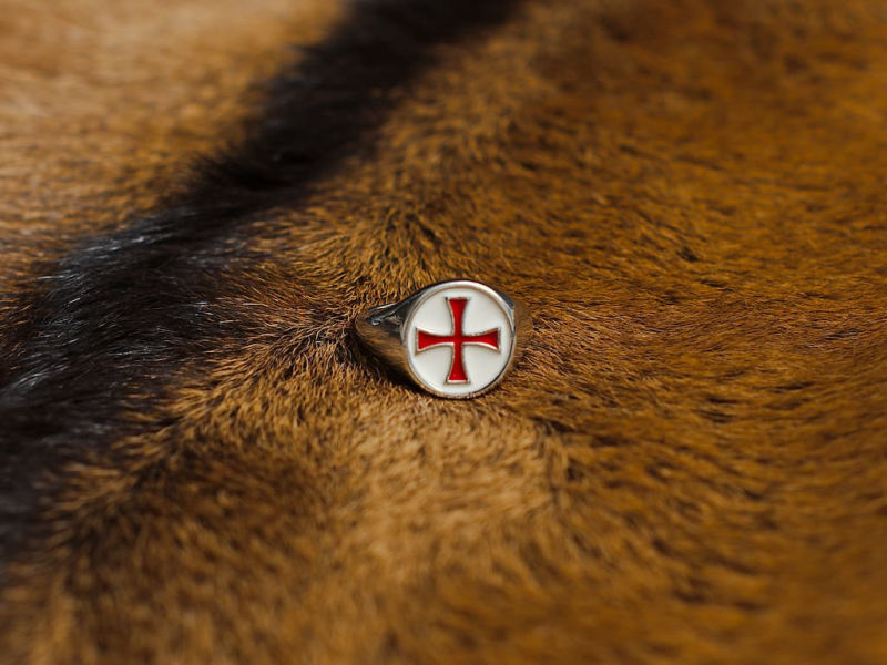 Épée templière de décoration posée sur une table médiébale en bois, avec une branche dont les branches abritent des gouttes de rosée Bague croix templière rouge cerclée #Terressens